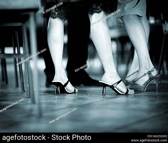 Feet and legs of young women wedding guest in high heel shoes and cocktail party dress in wedding reception blue black and white toned photo