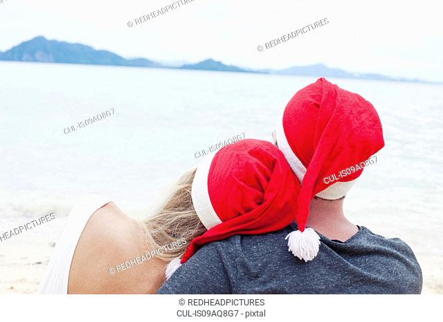 Rear view of young couple wearing santa hats on beach, Kradan, Thailand