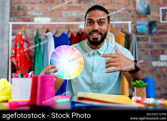 Mixed race male designer in sitting at desk holding a colour chart and smiling
