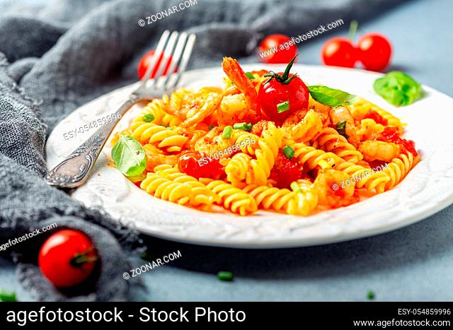 Delicious seafood Italian pasta fusilli with shrimp, cherry tomatoes and garlic served on a textured white plate, selective focus