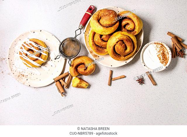 Homemade pumpkin cinnamon bun rolls sweet autumn baked dessert with cream cheese sauce in spotted ceramic plates with cinnamon sticks and vintage sieve over...