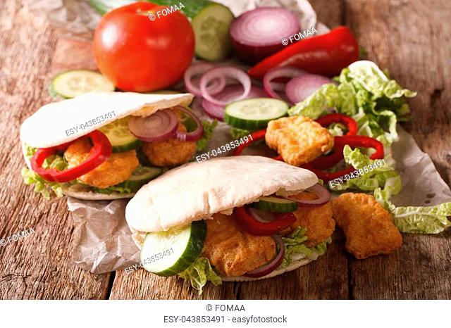 Tasty pita with chicken nuggets, cucumber, nappa cabbage, onion and bell peppers closeup on the table. horizontal