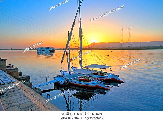 sailboats, feluccas on the banks of the Nile with river cruise ship at sunset, Karnak near Luxor, Upper Egypt, Egypt