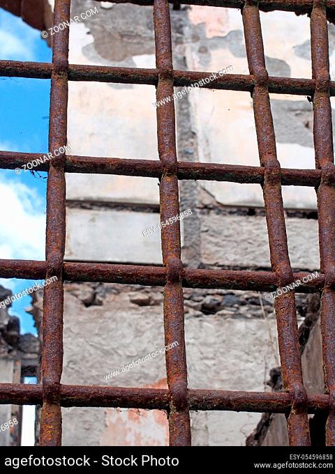 a close up of a rusting iron fence with bars in front of a ruined collapsing building