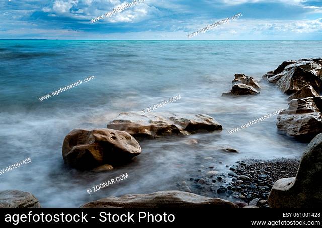 Seawaves splashing onto the sandy coast with pebbles and blue cloudy sky. Melanda coast , Pissouri Cyprus. Long exposure photography