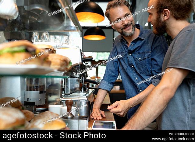 Smiling cafe owner talking to barista in coffee shop
