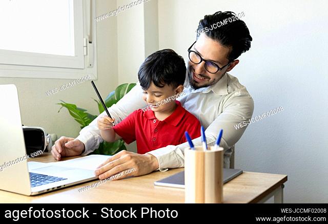 Businessman looking at laptop while sitting with son at home