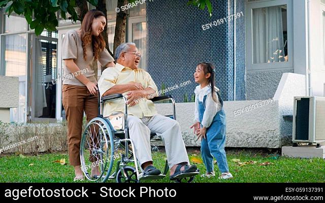 Disabled senior grandpa on wheelchair with grandchild and mother in park, Happy Asian three generation family having fun together outdoors backyard
