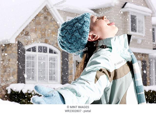 Winter snow. A girl holding out her arms with her head back, catching the falling snow in her open mouth