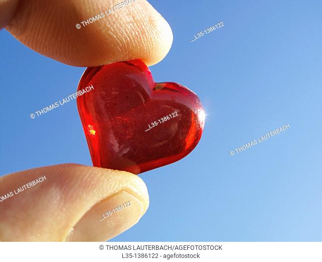 Hand holding small glass heart with blue sky