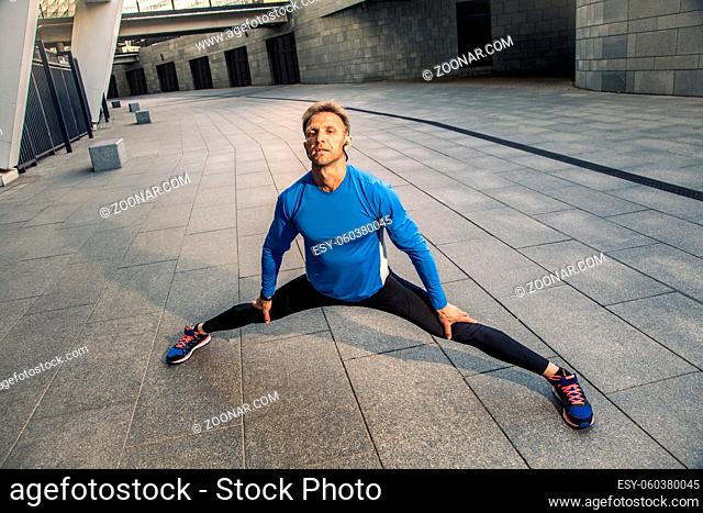 Handsome athlete man in black blue sport uniform stretching body, warming up and get ready for jogging