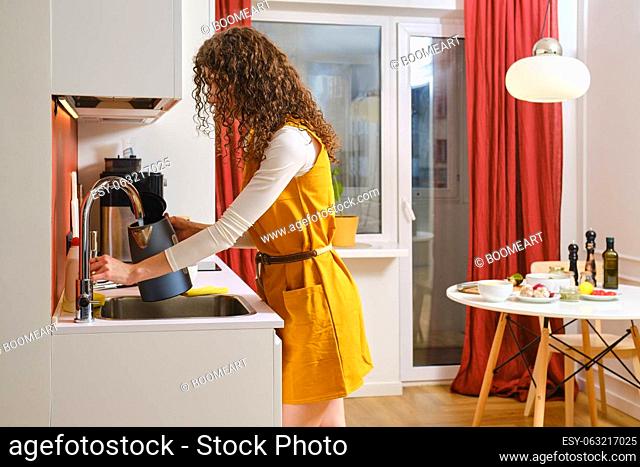 Young woman in the kitchen pours water from the tap into the kettle