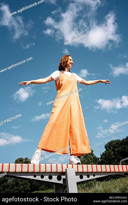 Young woman with arms outstretched standing on seesaw