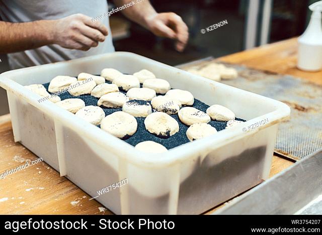 Baker putting black poppy seed on raw bread rolls