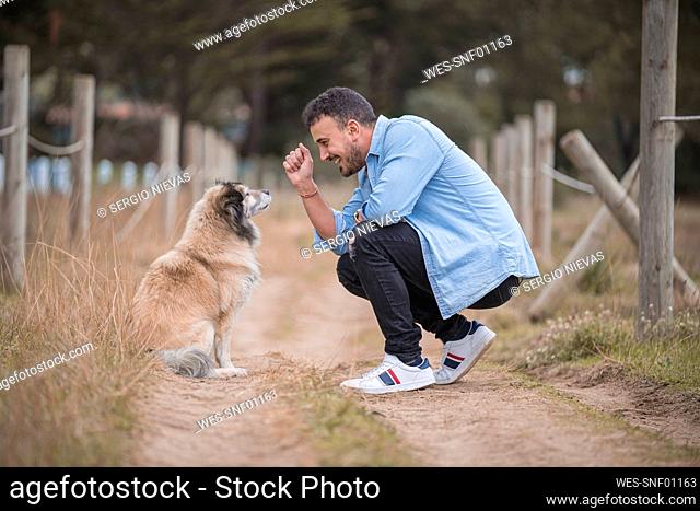 Smiling man with dog crouching on dirt road