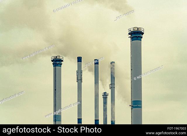 Tall factory smokestacks emitting smoke in sky