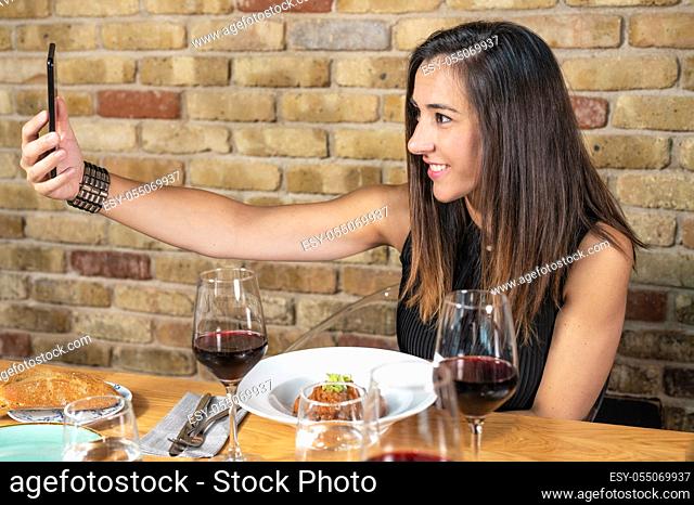 Beautiful Young woman is taking a selfie photograph while eating in restaurant. High quality photo