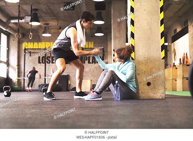Athlete helping young woman getting up after a break in gym