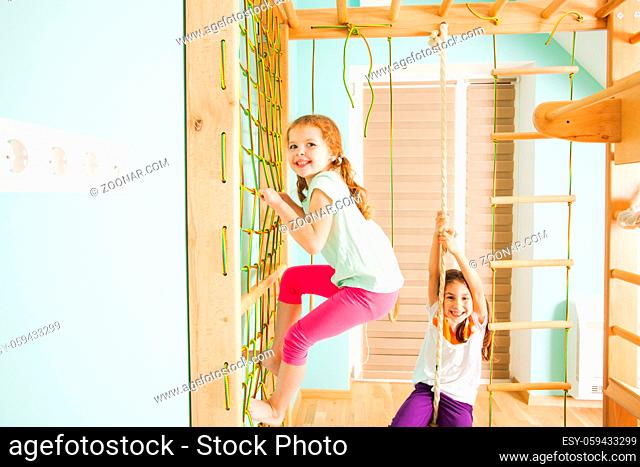 Happy smiling siblings boy and girl swinging on a wooden ladder and swing on sports complex. Close view of brother and sister happily playing on a kids gym in...