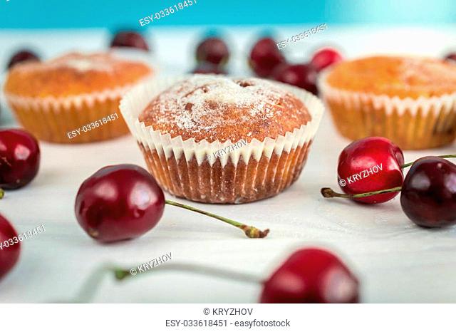 Macro shot of freshly baked muffins decorated by cherries on wooden table