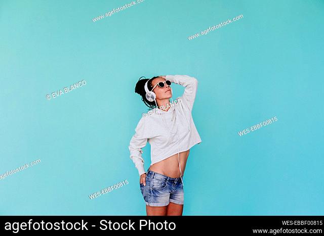 Fashionable mid adult woman listening music while looking up against turquoise background