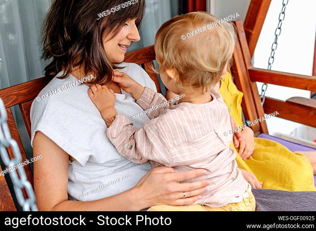 Close up of mother with her little son and daughter sitting on terrace swing