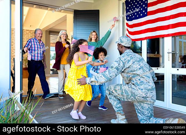 Multiracial excited multigeneration family with flag of america welcoming army soldier in house