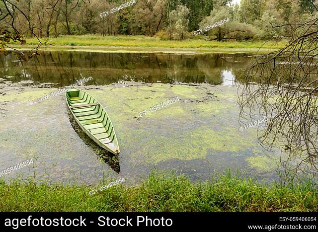 view of traditional metal boat moored in oxbow lake at Ticino river , shot in a bright cloudy fall day in Ticino park near Bernate, Milan, Lombardy, Italy