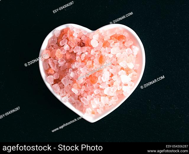 Himalayan pink salt in hearth-shape bowl on black stone background. Copy space