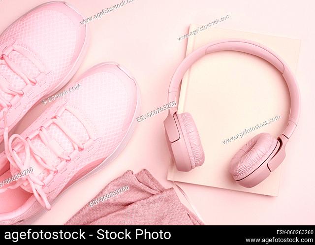 pink wireless headphones, a pair of sneakers and a notepad on a beige background, top view. Womens clothing