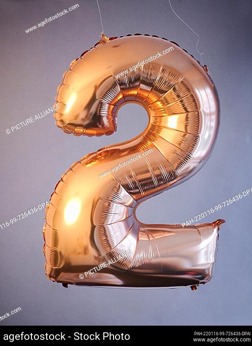 PRODUCTION - 14 January 2022, Berlin: ILLUSTRATION - A golden balloon in the shape of the number 2 hangs against a gray background