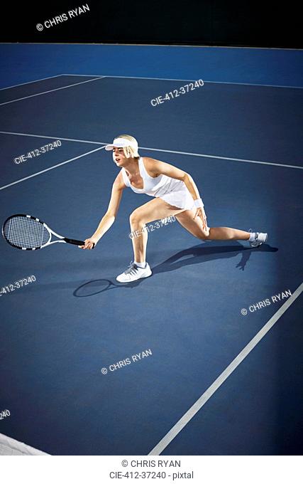 Young female tennis player playing tennis, reaching with tennis racket on blue tennis court