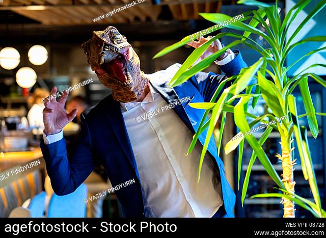 Male owner gesturing while wearing dinosaur mask at cafe