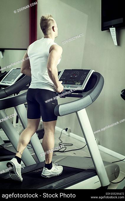 Blond attractive young man running on treadmill, seen from the back