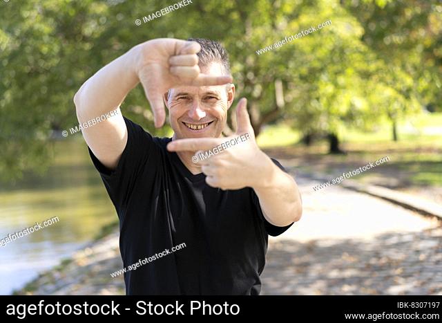 A handsome mature man looks through a frame made up of hands. Attractive man make frame by fingers, isolated on blur background with copy space for text