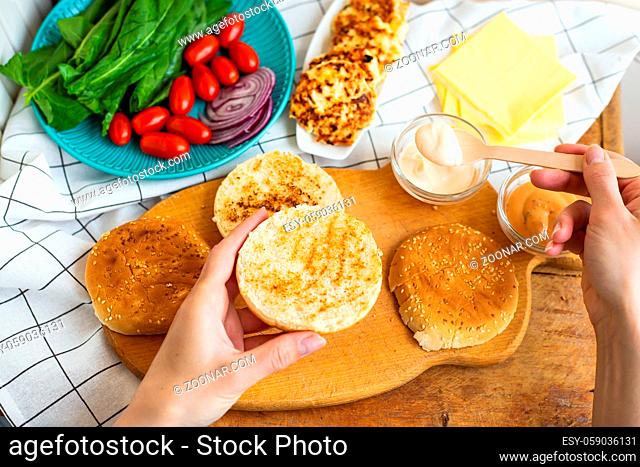 Preparation of all the ingredients for making a burger - bun, cutlet, cheese, salad, tomato, sauces. Top view, girl's hands take a burger roll