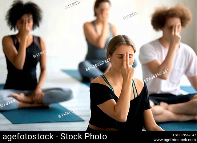 Group of multi ethnic people sitting cross-legged on floor doing yoga practice Alternate Nostril Breathing, exercise reduces stress anxiety