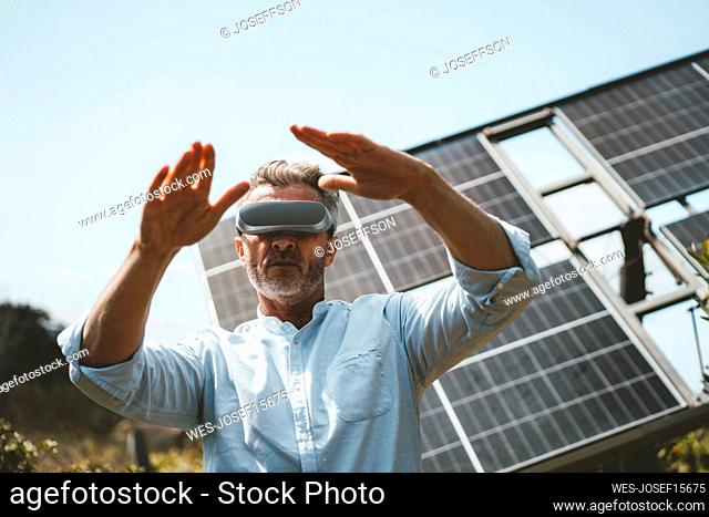 Mature man gesturing with futuristic glasses in front of solar panels