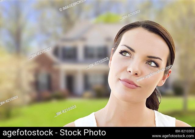 Thoughtful pretty mixed-race woman in front of house looking up and to the side