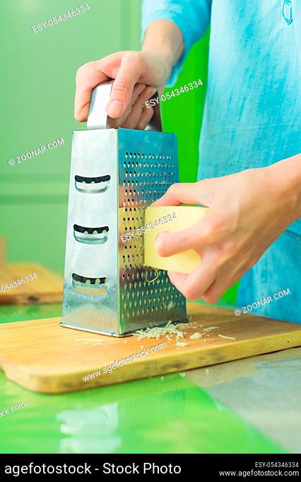 Close-up of a woman's hands rub a parmesan cheese on a metal grater on a green table