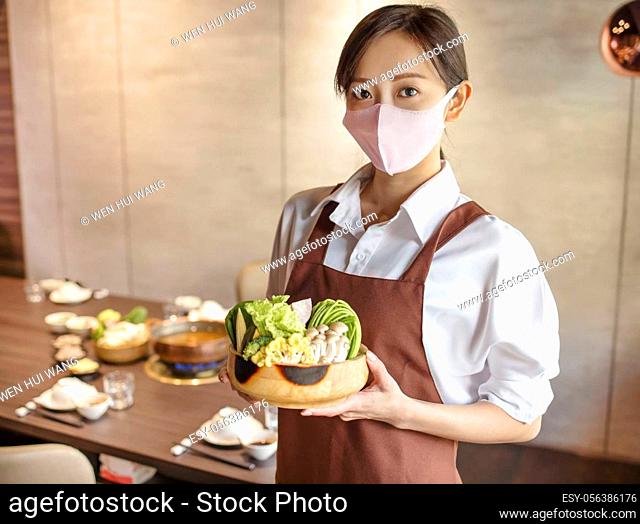 Young waiter wearing protective face mask while serving food to customer in restaurant