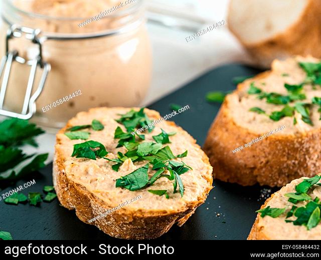 Close up view of slice bread with homemade turkey pate and fresh green parsley on black kutting board over white concrete background, Shallow DOF