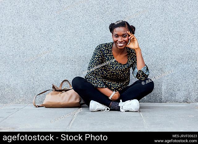 Smiling woman sitting cross-legged on footpath
