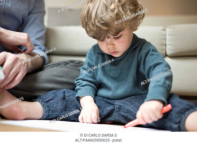 Toddler boy sitting on floor with father, drawing on paper