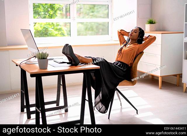 Side view of relaxed young businesswoman sitting feet up at office desk