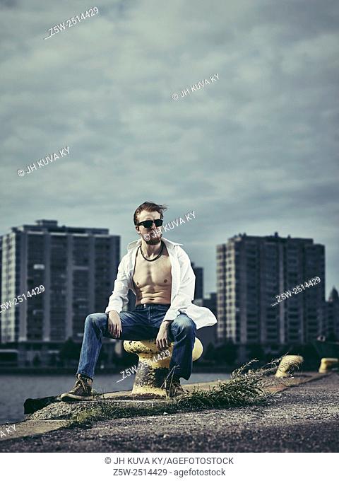 Handsome man wearing white shirt and jeans, windy day in harbour
