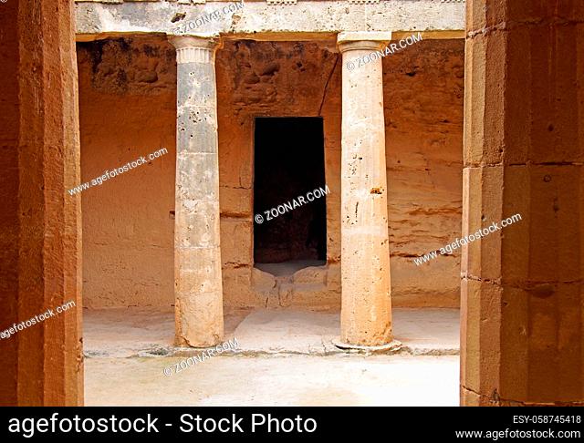 an underground chamber at the tombs of the kings in paphos cyprus with old eroded sandstone columns surrounding a dark empty doorway
