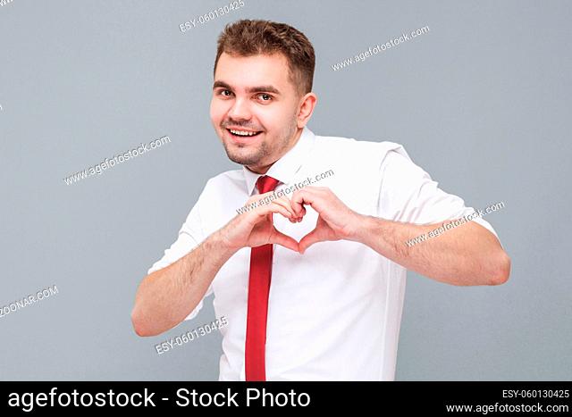 I love you. Portrait of young handsome happy man in white shirt and tie standing with heart love shape with hands and looking at camera with happy face