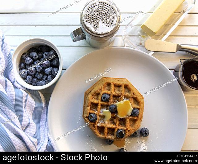 Begian waffles with fresh blueberries, butter. and pure maple syrup on a white natural wood table top view