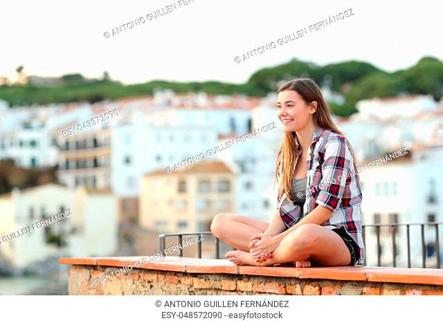 Happy teen contemplating views sitting on a ledge in a coast town on vacation